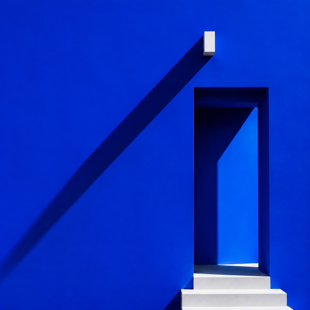 A sharp geometric architectural blue wall casting long minimal shadows under intense cobalt sunlight