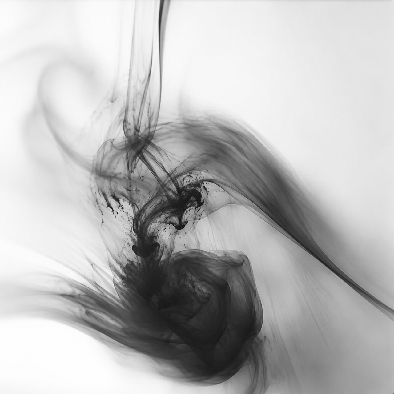 Black smoke curls and disperses across a plain white ground in a monochrome image.